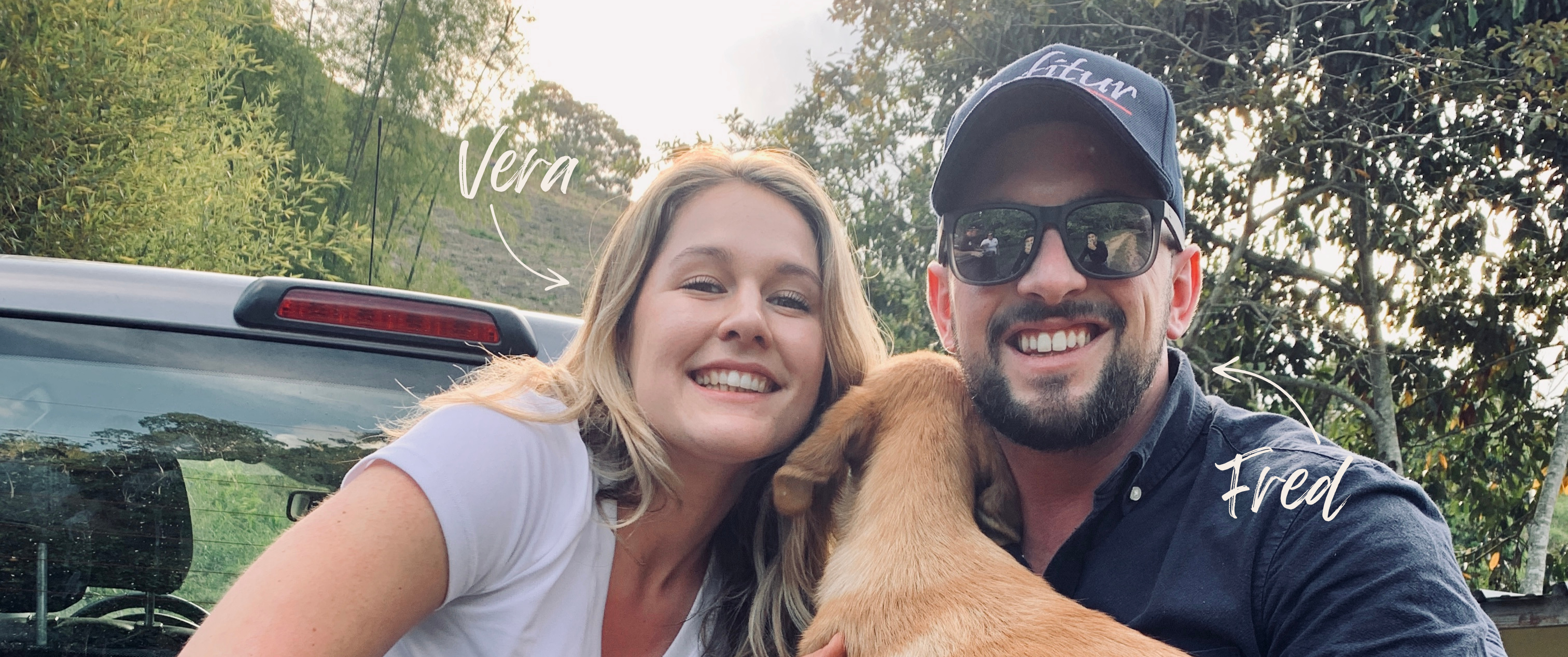 Vera Richartz und Frederic Bertolone lachen auf der Ladefläche eines Pickups mit einem Hund im Arm – fröhlicher Moment auf einer Kaffeefarm während der Cofitur-Reise in Huila, Kolumbien
