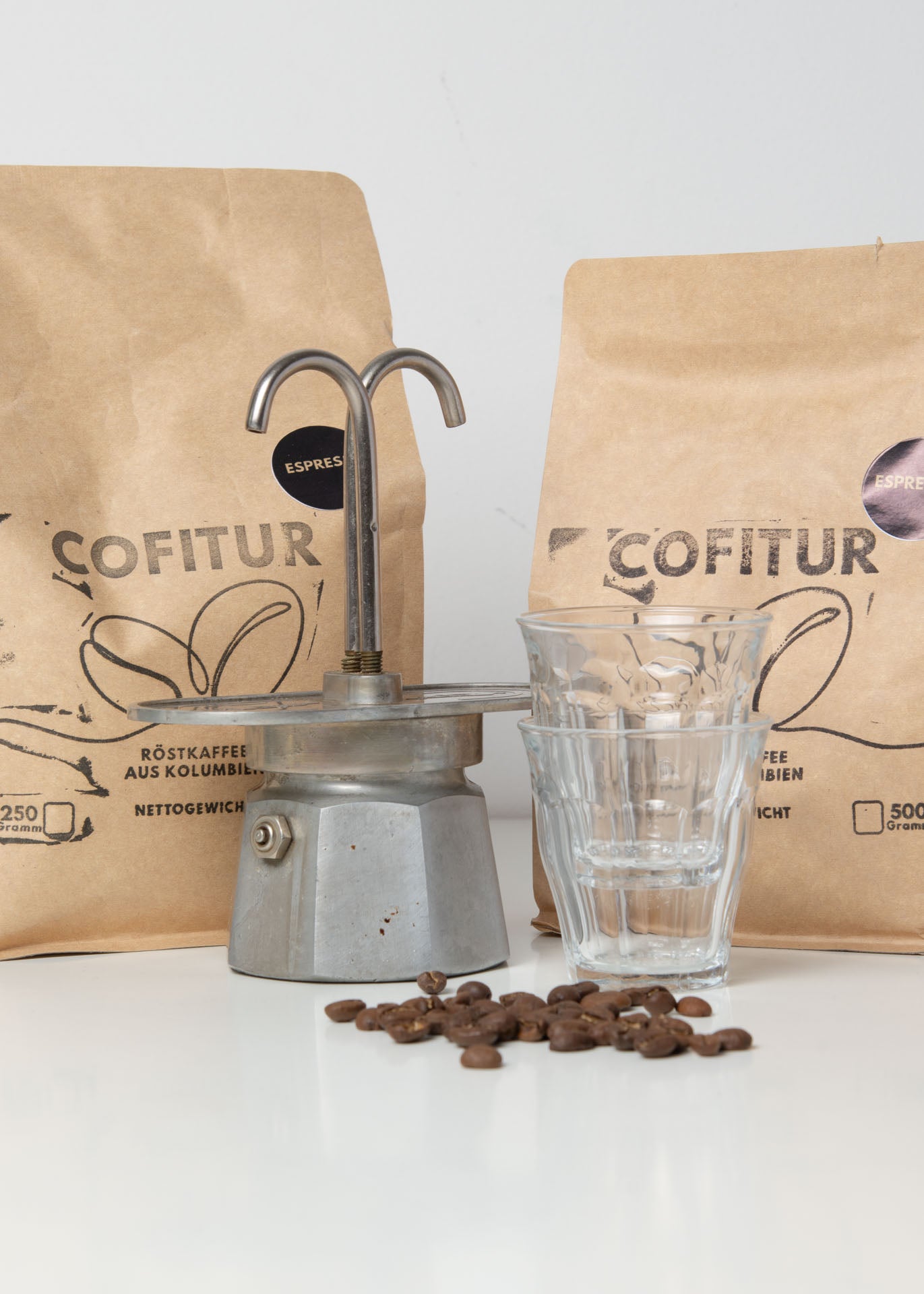 Cofitur Espressobohnen in Papiertüten neben einem kleinen Espressokocher – stimmungsvolle Szene zur Zubereitung kolumbianischen Kaffees