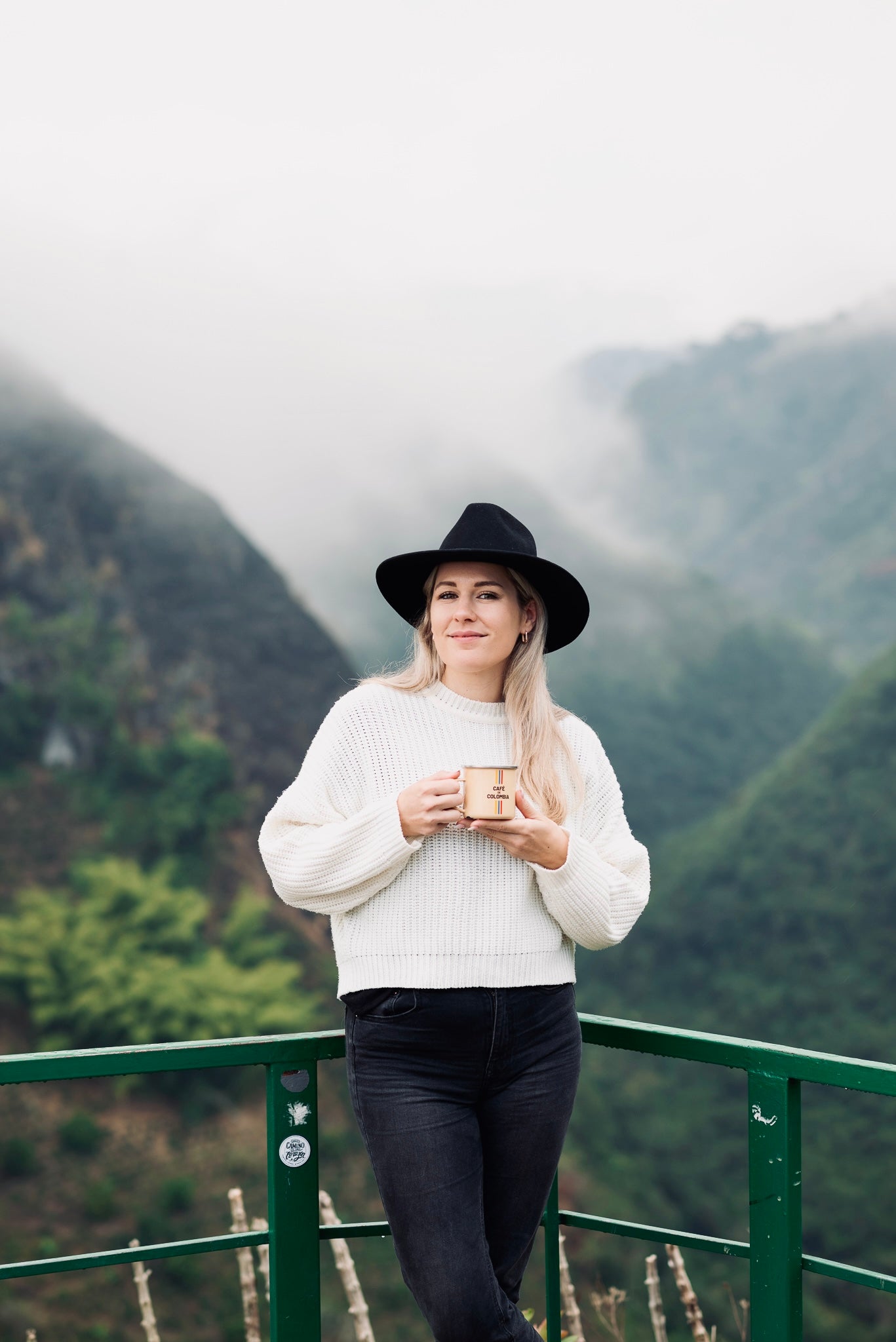 Vera Richartz mit Kaffeetasse und Hut an der Rehling bei La Chaquira in Huila – kraftvoller Blick vor Nebelwald und Kaffeelandschaft, Sinnbild für Verbundenheit und Verantwortung